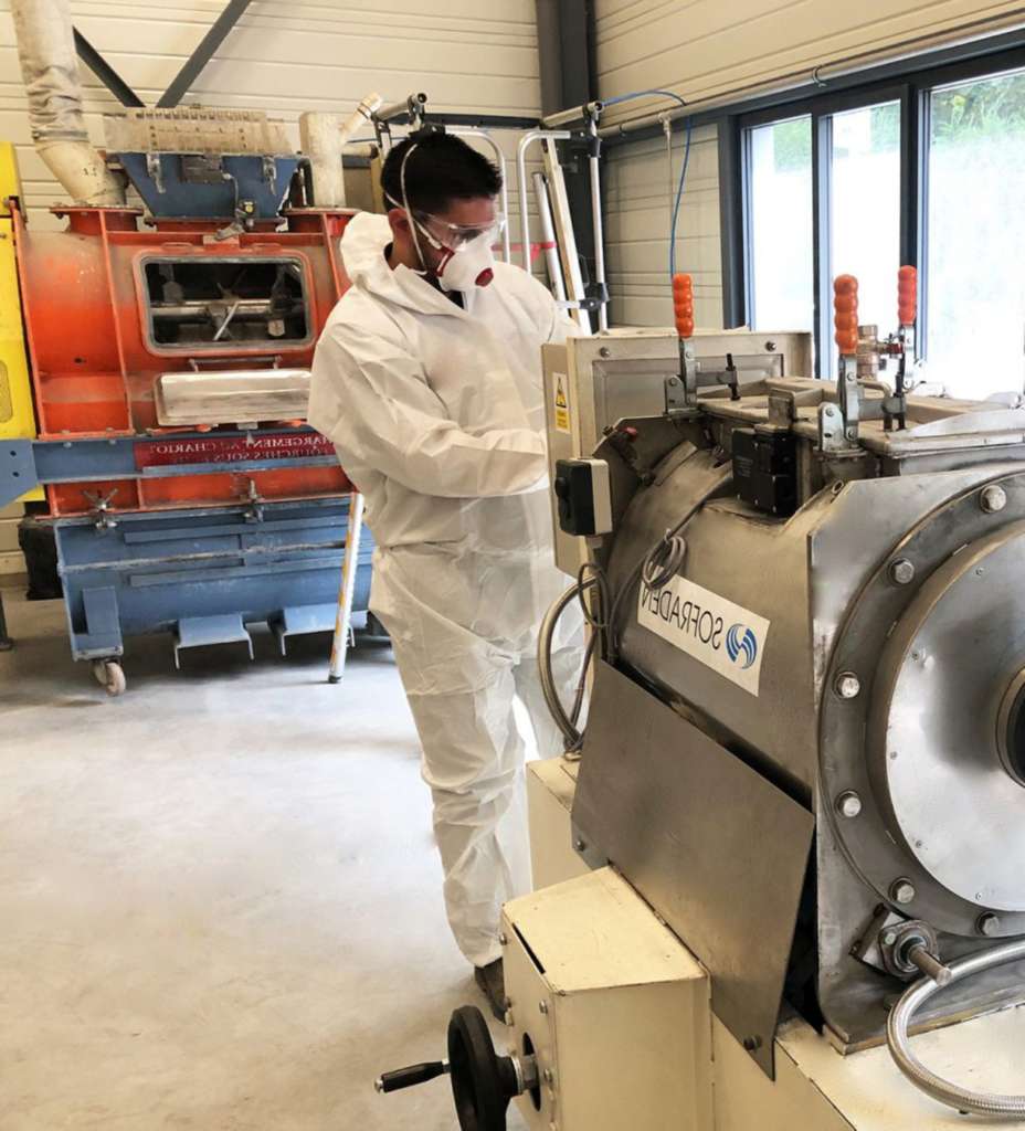 Un homme portant un masque respiratoire et des vêtements de protections en train d'inspecter un mélangeur industriel